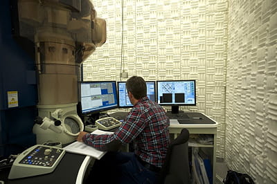 un opérateur, à l'intérieur d'une zone insonorisée, opère un microscope